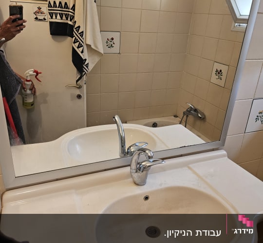 בקבוק תרסיס ניקוי מוחזק ביד ליד כיור במקלחת